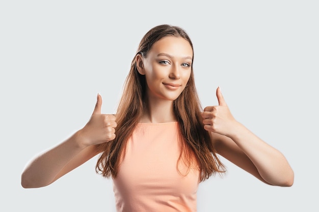 Linda garota sorrindo e mostra os polegares para cima gesto com as duas mãos em um fundo branco isolado Mulher positiva aponta para uma ideia um lugar para publicidade