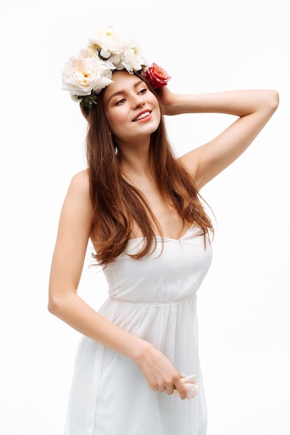 Linda garota sorrindo e posando com flores na parede branca em retrato de vestido branco