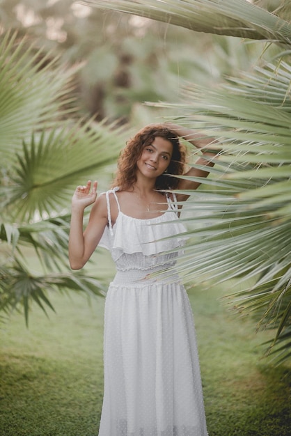 Linda garota sorrindo perto de palmeiras em um vestido branco