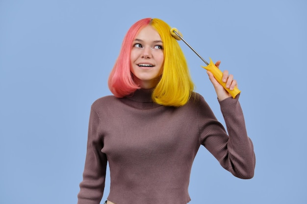 Linda garota tinge o cabelo com rolo de construção, adolescente com penteado rosa amarelo colorido na moda. Coloração, salão, moda, penteados, conceito de beleza, fundo de estúdio de cor azul