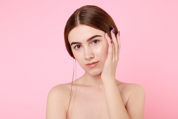 Linda garota tocando sua pele perfeita no fundo rosa. Conceito de cuidados com a pele. Retrato de mulher de beleza com pele limpa. Beleza fofa modelo com maquiagem natural em fundo rosa