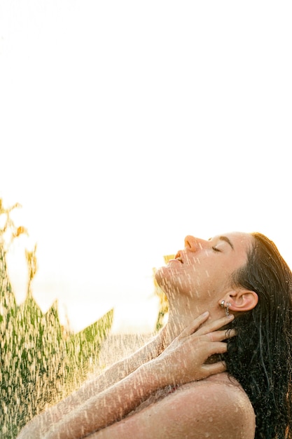 Linda garota toma uma ducha tropical ao ar livre ao pôr do sol. cuidados de higiene e beleza. tratamentos de água de spa.