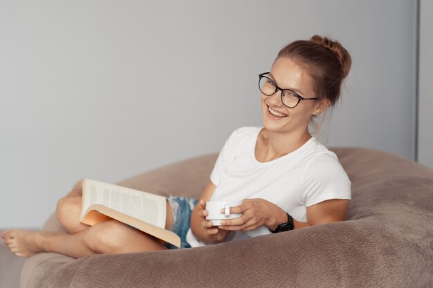 Linda garota tomando café e lendo um livro em casa