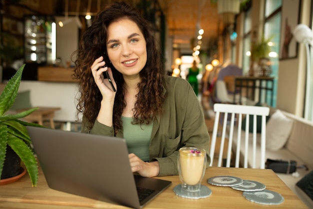 Linda garota trabalhando em uma cafeteria com uma freelancer mulher laptop segurando um telefone conectado à internet através do computador, fazendo compras online