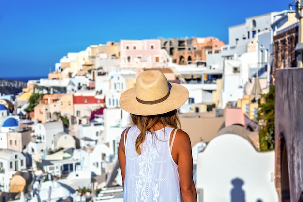 Linda garota turista de chapéu de palha contra a vila de Oia com famosas casas brancas e igrejas azuis na ilha de Santorini, mar Egeu, Grécia Conceito de viagem
