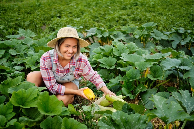 Linda garota usando chapéu, escolhendo as mais frescas abobrinhas e abobrinhas em um jardim. Colheita De Vegetais De Outono.