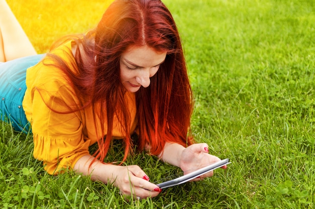 Linda garota, usando um computador tablet em um parque verde frondoso, navegando a tela sensível ao toque