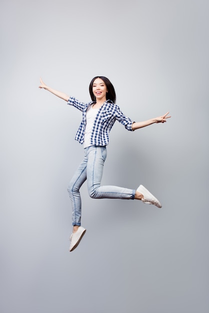 Linda garota vestida com camisa xadrez e jeans, pulando e mostrando vsign