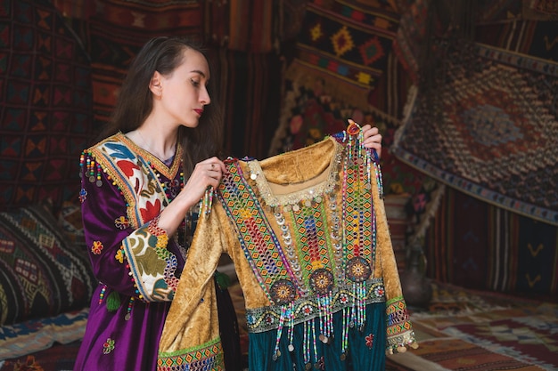 Linda garota vestida com roupas nacionais turcas na sala com o interior há muitos tapetes nas paredes