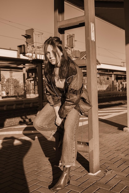 Linda garota vestida no estilo dos anos 90 com receptor de rádio portátil nas mãos posando na plataforma da estação de trem