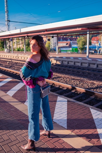 Foto linda garota vestida no estilo dos anos 90 com receptor de rádio portátil nas mãos posando na plataforma da estação de trem