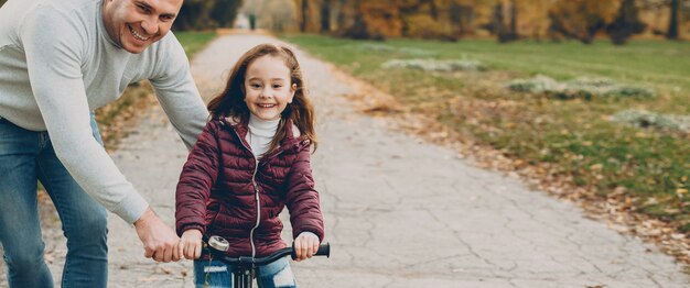 Linda garotinha aprendendo a andar de bicicleta com o pai ao ar livre no parque.