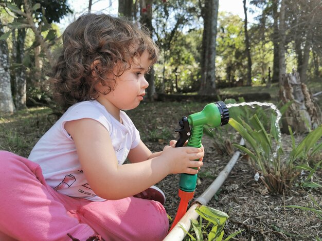 Linda garotinha brasileira se divertindo brincando com a mangueira de água no jardim.