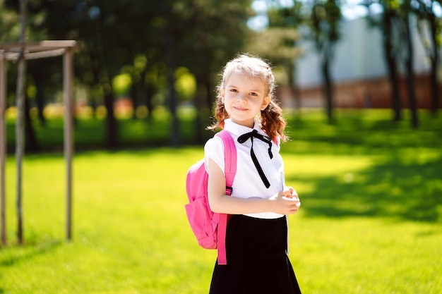 Linda garotinha com mochila andando no parque pronto para voltar para a escola, cair ao ar livre, o conceito de educação