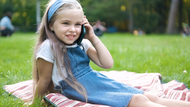 Linda garotinha conversando em seu celular no parque de verão