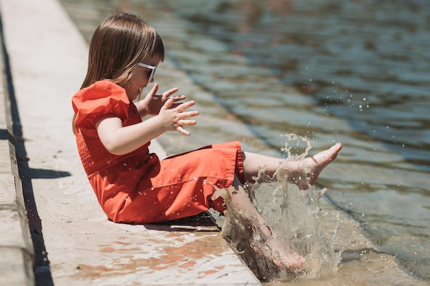 linda garotinha de vestido vermelho e com óculos brincando ao ar livre com água