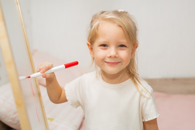 linda garotinha em casa desenha com caneta hidrográfica na lousa