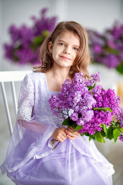 Linda garotinha em idade pré-escolar em um vestido delicado sentada em um balanço decorado com flores lilás