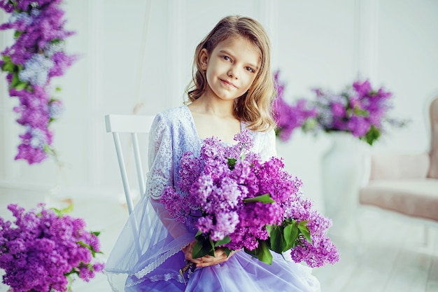 Linda garotinha em idade pré-escolar em um vestido delicado sentada em um balanço decorado com flores lilás