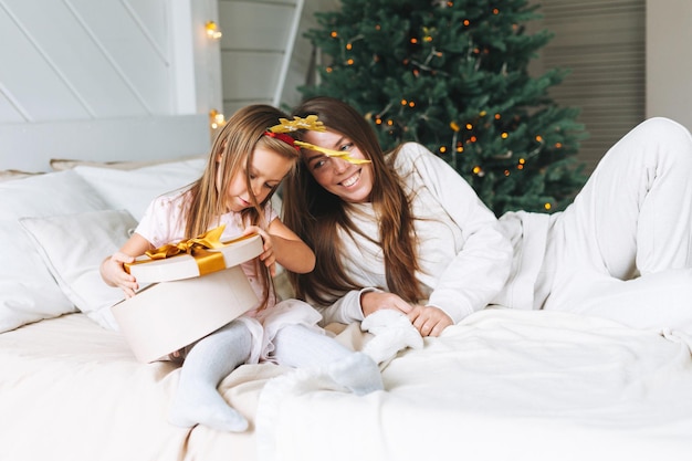 Linda garotinha engraçada com a mãe na cama no quarto com árvore de natal