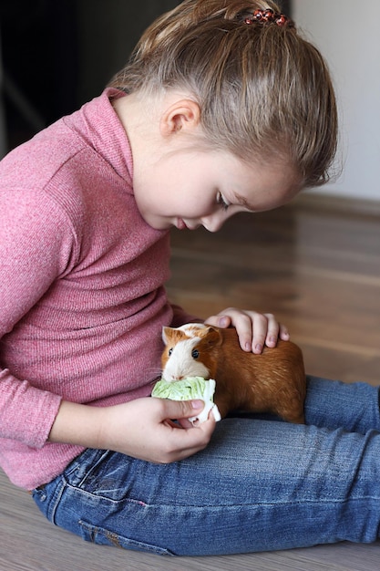 Linda garotinha está alimentando sua adorável cobaia Conceito de cuidados com animais crianças com animais de estimação