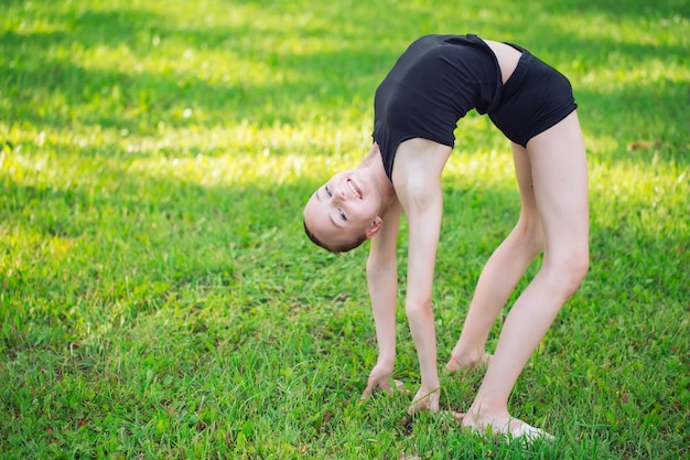 Linda garotinha fazendo ginástica na grama em um dia ensolarado