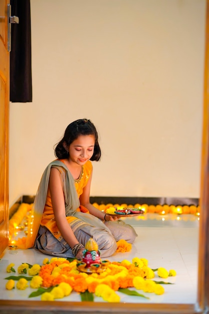 Linda garotinha indiana fazendo decoração com flor e lâmpada de óleo para o festival de diwali em casa.