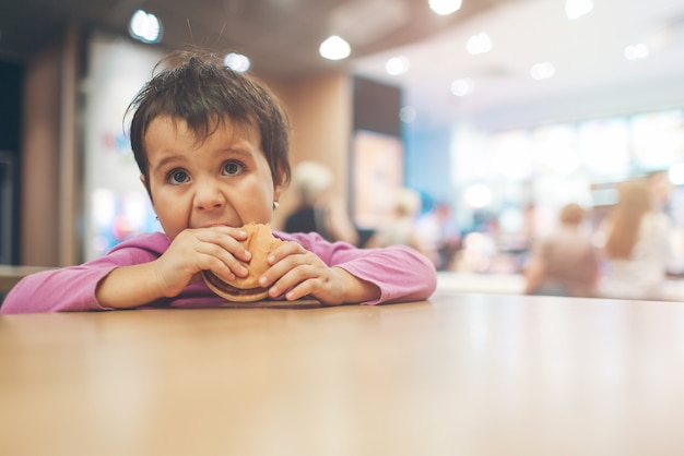 Foto linda garotinha latina comendo um hambúrguer e olhando para o espaço da cópia