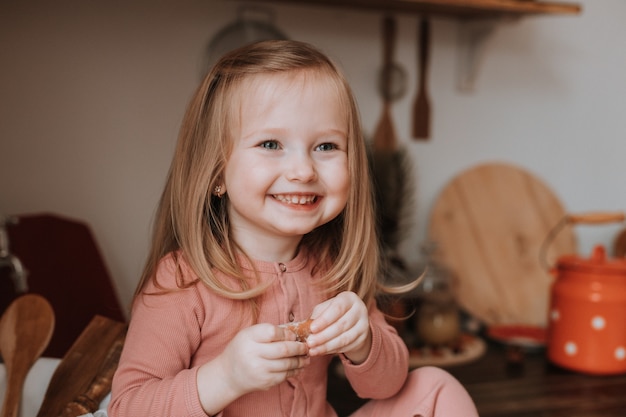 linda garotinha loira de pijama rosa comendo biscoitos na cozinha, lanche saudável para crianças