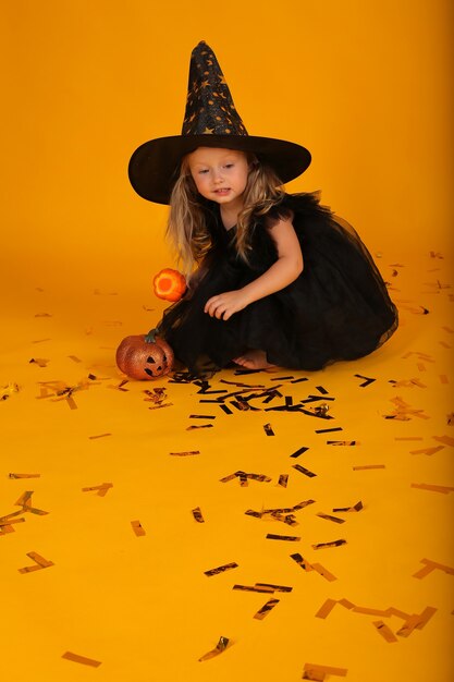 Foto linda garotinha loira em um vestido preto e um chapéu de bruxa.