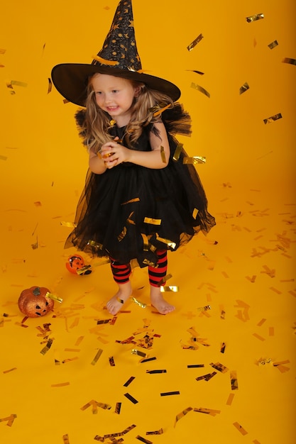 Foto linda garotinha loira em um vestido preto e um chapéu de bruxa.