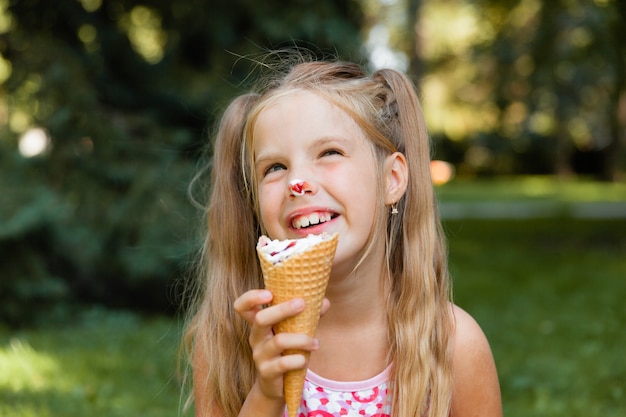 Linda garotinha loira tomando sorvete no verão no parque. garota alegre com sorvete.