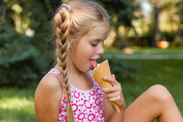 Linda garotinha loira tomando sorvete no verão no parque. garota alegre com sorvete.