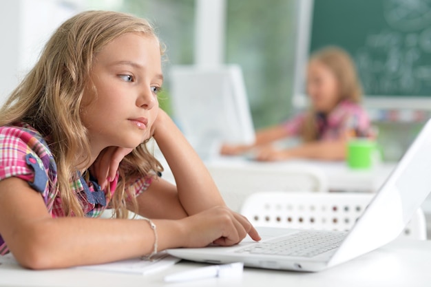 Linda garotinha na sala de aula trabalhando com laptop