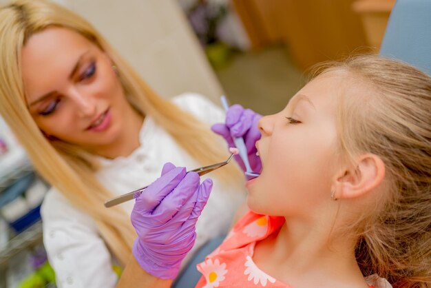 Linda garotinha na visita no consultório do dentista. Ela está sentada em uma cadeira e dentes de checkup feminino dentista nela. Foco seletivo.