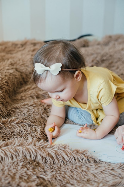 Linda garotinha segurando giz de cera amarelo e inclinando-se para o caderno de desenho na frente dela