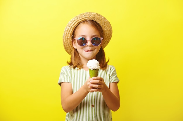 Linda garotinha segurando um sorvete e vai comê-lo, lambendo os lábios, vestida com um vestido de verãob