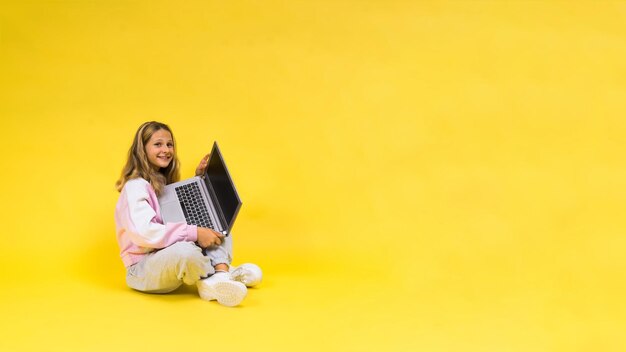 Linda garotinha sentada em um piso claro com um laptop cinza e sorrindo espaço vazio