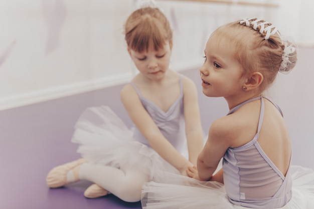 Linda garotinha, sentada no chão com sua melhor amiga na escola de ballet