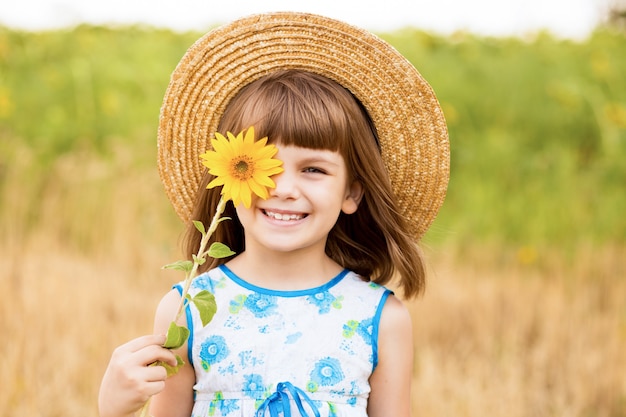 linda garotinha sorri e esconde os olhos com uma flor de girassol caminhando ao ar livre no feriado de primavera