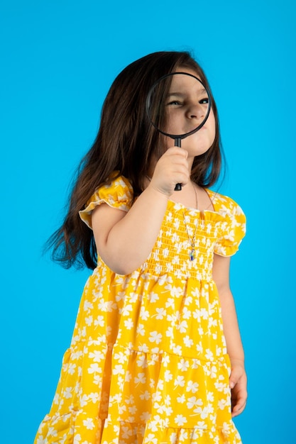 Linda garotinha sorridente com uma cara engraçada em um vestido amarelo listrado posando em um fundo azul no estúdio