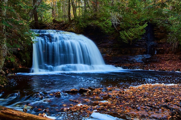 Linda grande cachoeira azul com bacia e riacho fluindo sobre rochas com folhas caídas e floresta