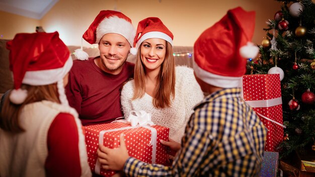 Linda hermana y hermano sosteniendo cajas de regalo para sus padres para Navidad o Año Nuevo en casa. Enfoque selectivo. Centrarse en el fondo, en los padres.