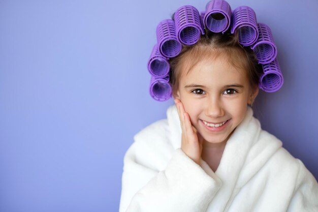 Linda hermosa chica de belleza en una bata de baño blanca con el pelo rizado en rulos sonríe dulcemente