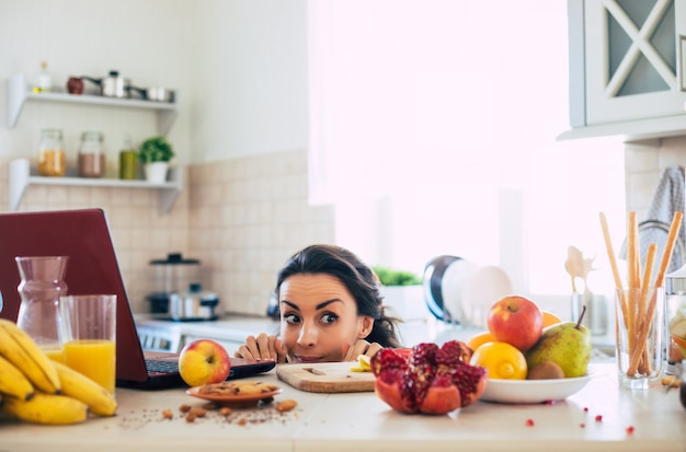 Linda hermosa y feliz joven morena en la cocina de casa está mirando frutas