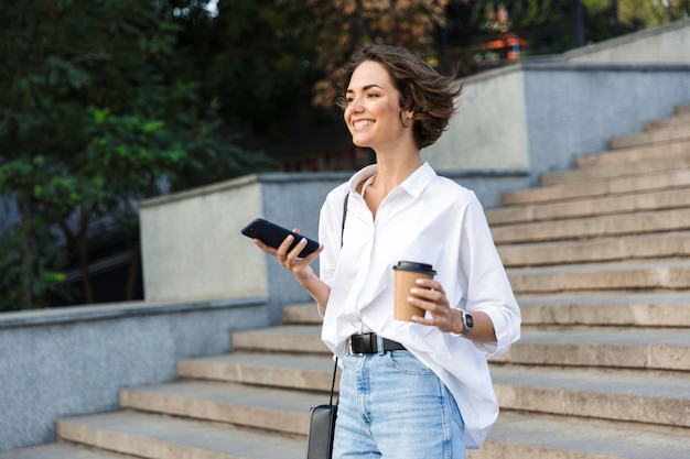 Linda hermosa mujer caminando por la calle con teléfono móvil con café