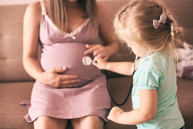 Linda hija jugando al doctor y comprobando a la madre embarazada