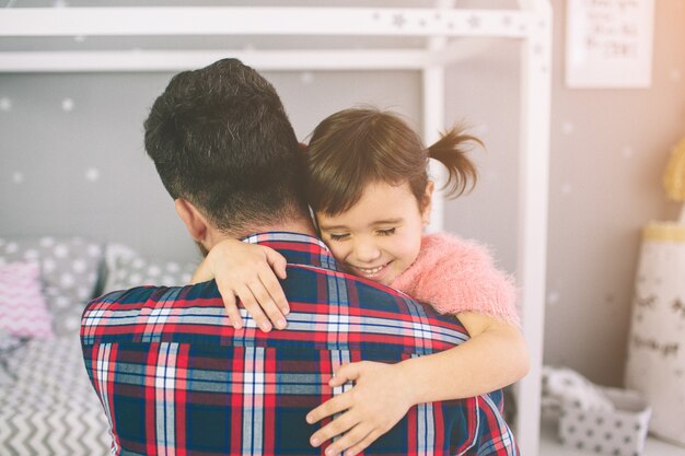 Linda hijita y su apuesto joven papá están jugando juntos en la habitación del niño. Papá e hijo pasan tiempo juntos mientras están sentados en el suelo de la habitación.