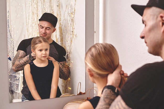 Linda hijita y su papá tatuado están jugando juntos cerca de un espejo papá está haciendo su hija ...