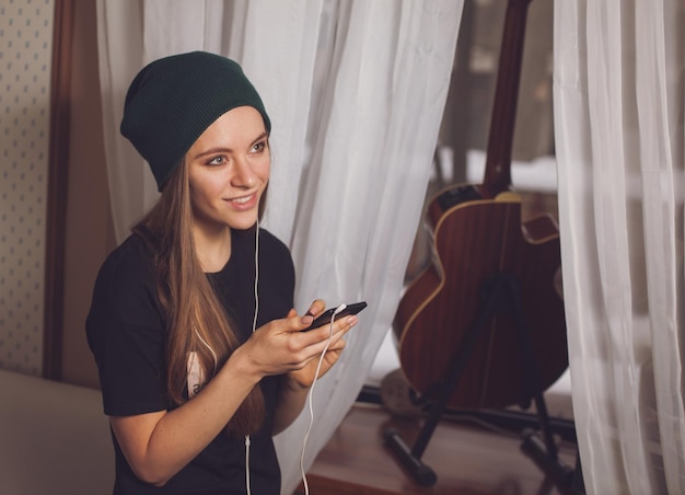 Linda hipster mujer escuchando música cerca de la guitarra